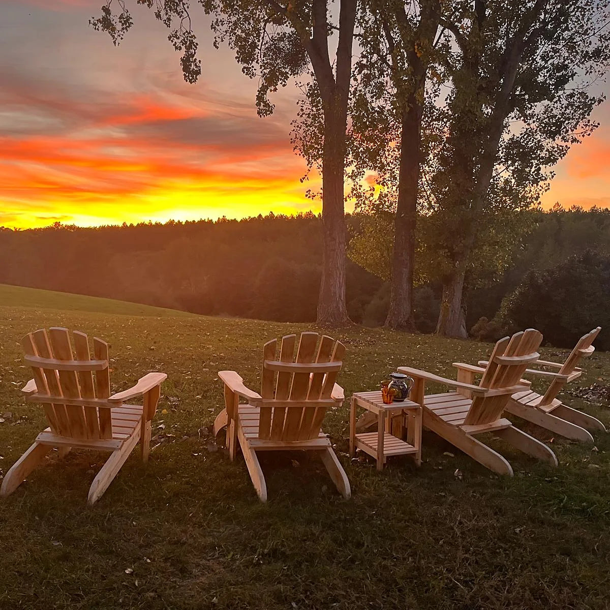 Quatre fauteuils Adirondack et une table en cèdre installés dans un pré au coucher du soleil