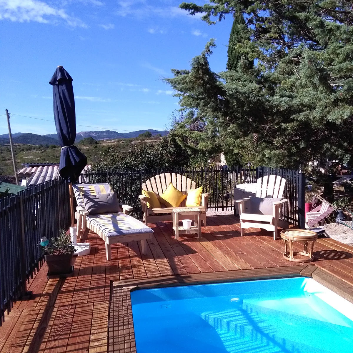 Salon de jardin en cèdre, fauteuils, banc et chaise longue installés au bord d'une piscine